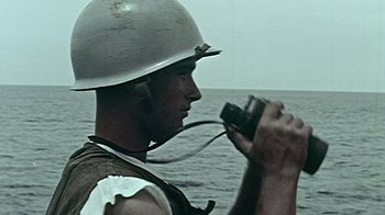 Movie still from “The Fog of War” (2003), directed by Errol Morris – A man holding a camera while standing in front of a body of water; Close Up shot, High angle