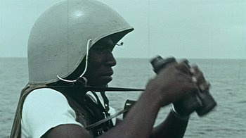 Movie still from “The Fog of War” (2003), directed by Errol Morris – A man wearing a helmet is holding a camera; Close Up shot, High angle