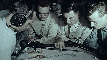 Movie still from “The Fog of War” (2003), directed by Errol Morris – A group of men sitting around a table working; Medium shot, High angle