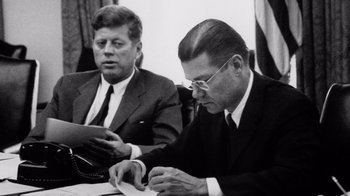 Movie still from “The Fog of War” (2003), directed by Errol Morris – Two men sitting at a table and one is writing something; Close Up shot, Over the shoulder angle