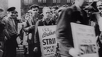 Movie still from “The Fog of War” (2003), directed by Errol Morris – A group of men standing next to each other holding signs; Medium shot, High angle