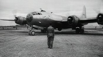 Movie still from “The Fog of War” (2003), directed by Errol Morris – A man standing in front of an airplane on a field; Wide shot, Low angle