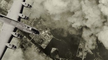 Movie still from “The Fog of War” (2003), directed by Errol Morris – An aerial view of an airplane flying over a city; Extreme Wide shot, Overhead angle