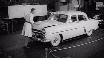 Movie still from “The Fog of War” (2003), directed by Errol Morris – An old photo of a man working on an old car; Wide shot, Low angle