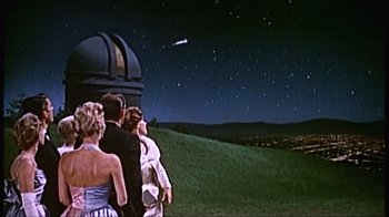 Movie still from “The Fog of War” (2003), directed by Errol Morris – A group of people standing on top of a green hill; Extreme Wide shot, Low angle