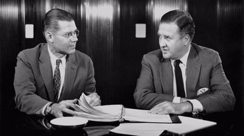 Movie still from “The Fog of War” (2003), directed by Errol Morris – Two businessmen sitting at a table with papers in front of them; Medium shot, Low angle