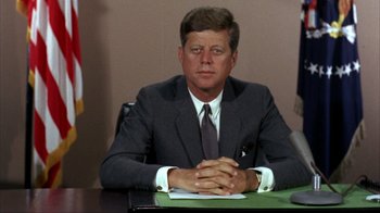 Movie still from “The Fog of War” (2003), directed by Errol Morris – A person sitting at a table wearing a suit; Close Up shot, Low angle