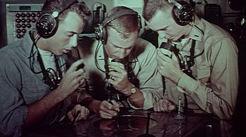 Movie still from “The Fog of War” (2003), directed by Errol Morris – A group of men sitting around a table with microphones; Medium shot, High angle
