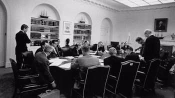 Movie still from “The Fog of War” (2003), directed by Errol Morris – A black and white photo of people sitting at a table; Wide shot, Over the shoulder angle