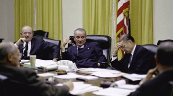 Movie still from “The Fog of War” (2003), directed by Errol Morris – Two men sitting at a table in front of a flag; Medium shot, Low angle