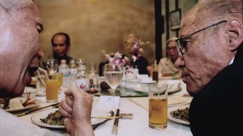 Movie still from “The Fog of War” (2003), directed by Errol Morris – A group of people sitting at a table with food; Close Up shot, Over the shoulder angle