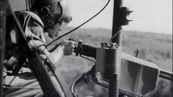 Movie still from “The Fog of War” (2003), directed by Errol Morris – A man in a helicopter holding a gun; Close Up shot, Low angle