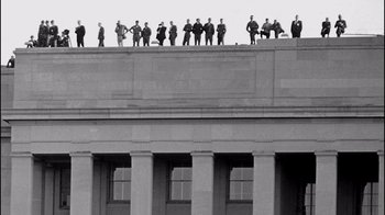 Movie still from “The Fog of War” (2003), directed by Errol Morris – A black and white photo of people standing on a building; Extreme Wide shot, Low angle