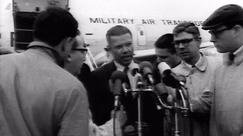 Movie still from “The Fog of War” (2003), directed by Errol Morris – A group of people standing around microphones on a stage; Medium shot, Over the shoulder angle