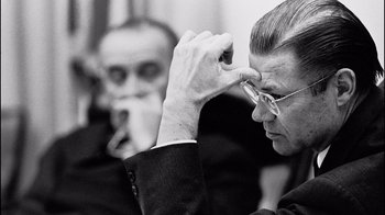 Movie still from “The Fog of War” (2003), directed by Errol Morris – A black and white photo of a man in a business suit; Close Up shot, Over the shoulder angle