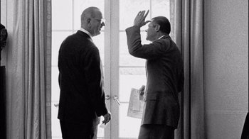 Movie still from “The Fog of War” (2003), directed by Errol Morris – Two men in suits are standing next to each other; Medium shot, Over the shoulder angle