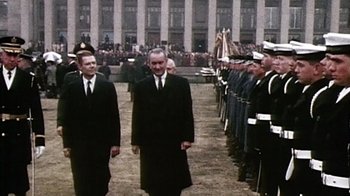 Movie still from “The Fog of War” (2003), directed by Errol Morris – A group of men in suits and ties standing in front of a crowd; Wide shot, Low angle