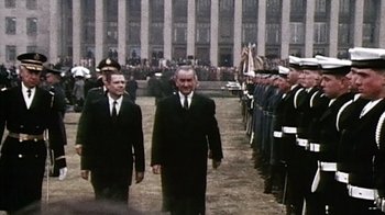 Movie still from “The Fog of War” (2003), directed by Errol Morris – Two men in suits walking in front of a crowd of people; Medium shot, High angle