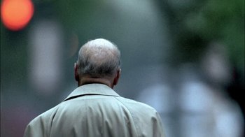 Movie still from “The Fog of War” (2003), directed by Errol Morris – An older man wearing a tan jacket walking down a street; Extreme Close Up shot, Low angle