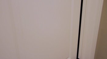 Movie still from “The Formula” (2014), directed by Thomas Beecher – A corner of a room with a white wall and black trim; Medium shot, High angle