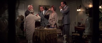 Movie still from “The Fortune” (1975), directed by Mike Nichols – A group of people standing around a table drinking wine; Wide shot, High angle