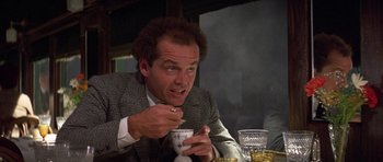Movie still from “The Fortune” (1975), directed by Mike Nichols – A man sitting at a table with a cup in his hand; Close Up shot, Low angle