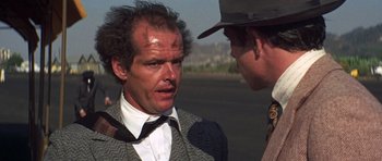 Movie still from “The Fortune” (1975), directed by Mike Nichols – A man in a suit and tie talking to another man in a hat and tie; Close Up shot, Over the shoulder angle
