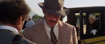 Movie still from “The Fortune” (1975), directed by Mike Nichols – A man wearing a suit and a hat; Close Up shot, Over the shoulder angle
