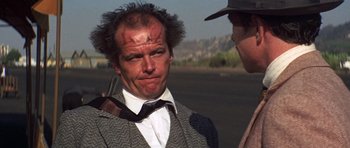 Movie still from “The Fortune” (1975), directed by Mike Nichols – A man in a suit and tie standing next to another man in a hat; Close Up shot, Over the shoulder angle