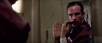 Movie still from “The Fortune” (1975), directed by Mike Nichols – A man in a suit and tie holding a pipe in front of a mirror; Close Up shot, Over the shoulder angle