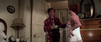 Movie still from “The Fortune” (1975), directed by Mike Nichols – A man holding a coffee mug and a knife; Medium shot, Low angle
