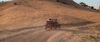 Movie still from “The Fortune” (1975), directed by Mike Nichols – An old car driving down a dirt road in the middle of the day; Extreme Wide shot, High angle
