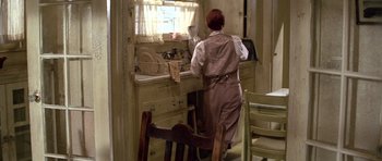 Movie still from “The Fortune” (1975), directed by Mike Nichols – A woman standing at a sink in a kitchen; Wide shot, High angle