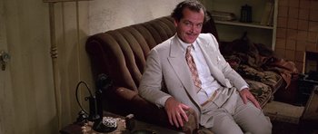 Movie still from “The Fortune” (1975), directed by Mike Nichols – A man sitting on a couch wearing a suit and tie; Medium shot, High angle