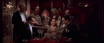 Movie still from “The Fortune” (1975), directed by Mike Nichols – A group of people sitting around a table with a cake; Medium shot, High angle