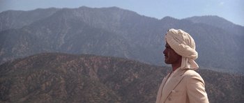 Movie still from “The Fortune” (1975), directed by Mike Nichols – A man in a turban standing on top of a mountain; Medium shot, Low angle