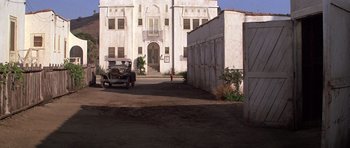 Movie still from “The Fortune” (1975), directed by Mike Nichols – An old car is parked in front of a building; Extreme Wide shot, Low angle
