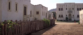 Movie still from “The Fortune” (1975), directed by Mike Nichols – An old white building with a wooden fence in front of it; Extreme Wide shot, Low angle