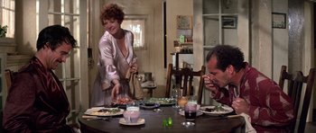 Movie still from “The Fortune” (1975), directed by Mike Nichols – A woman standing at a table with a plate of food; Medium shot, Over the shoulder angle