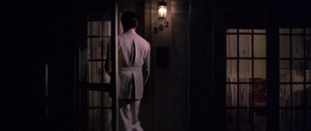 Movie still from “The Fortune” (1975), directed by Mike Nichols – A man in a suit standing next to a door way; Wide shot, High angle