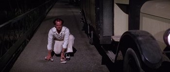 Movie still from “The Fortune” (1975), directed by Mike Nichols – A man kneeling down on the ground tying his shoes; Wide shot, High angle
