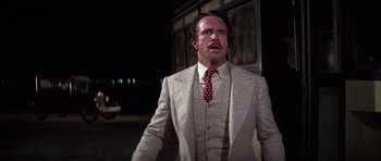 Movie still from “The Fortune” (1975), directed by Mike Nichols – A man wearing a suit and tie standing in front of a building at night; Medium shot, Low angle
