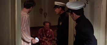 Movie still from “The Fortune” (1975), directed by Mike Nichols – A group of men standing next to each other in a living room; Medium shot, Over the shoulder angle