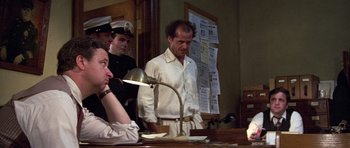 Movie still from “The Fortune” (1975), directed by Mike Nichols – A group of men standing around a table; Medium shot, Over the shoulder angle
