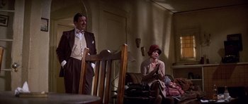 Movie still from “The Fortune” (1975), directed by Mike Nichols – A man and a woman sitting on a couch in a living room next to each other; Wide shot, Low angle