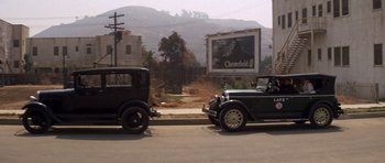 Movie still from “The Fortune” (1975), directed by Mike Nichols – Two old cars parked on the side of the road; Wide shot, High angle