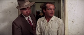 Movie still from “The Fortune” (1975), directed by Mike Nichols – A man in a hat and a man in a suit standing next to each other in a room; Close Up shot, Low angle