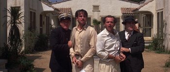 Movie still from “The Fortune” (1975), directed by Mike Nichols – A group of men standing next to each other in front of a building; Medium shot, Low angle