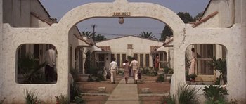Movie still from “The Fortune” (1975), directed by Mike Nichols – A group of people walking down a path in front of a building; Extreme Wide shot, Low angle