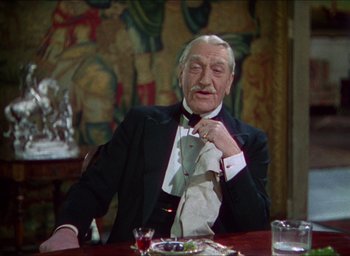 Movie still from “The Four Feathers” (1939), directed by Zoltan Korda – An older man sitting at a table with a tie; Medium shot, Over the shoulder angle
